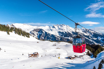 ski slope in Swiss Alps in sunny day. Red cable car above and mountains behind, skiing resort, Switzerland.