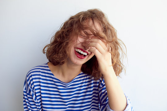 Laughing woman with curly hair on white wall