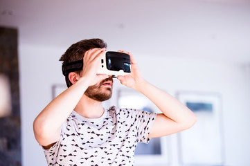 Man wearing virtual reality goggles, standing in living room