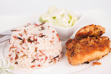 Pork chop (covered in breadcrumbs), three color rice and cucumber salad decorated with dill on a plate on white background