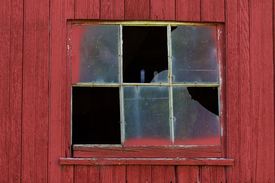 A Broken window on barn with red siding