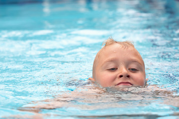 Fototapeta na wymiar A blond boy learning to swim in a swimming pool