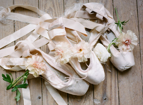 Close-up of ballet shoes with fresh flowers on wooden floor