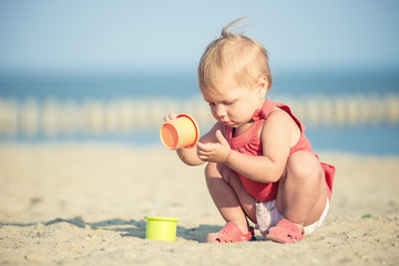 Baby playing on the sandy beach near the sea. Cute little girl in red dress with sand on tropical beach. Ocean coast.