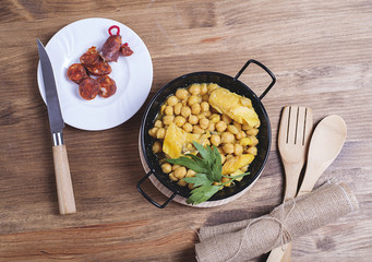 Close-up of nutritious chickpeas with codfish and sausage on plate.Fork and spoon.From above.