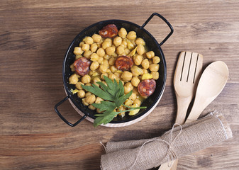 Close-up of nutritious chickpeas with codfish and sausage on plate.Fork and spoon.From above.