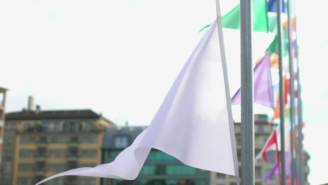 White flag waving in wind peacefully, street decorated with colorful banners