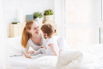 happy family mother and child playing and laughing in bed