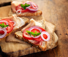 Sandwich with smoked ham, tomato, red onion and fresh oregano on a wooden board