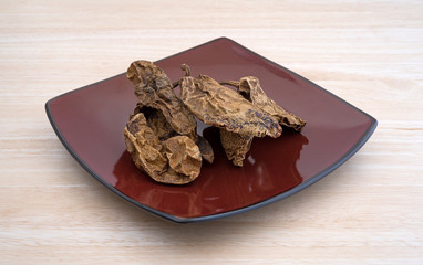 Dried chipotle chile peppers on a plate atop a wood table top.