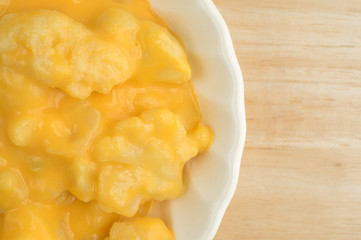 Serving of cauliflower with a cheese sauce in an old bowl top close view on table top.