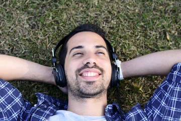 Young man listening to music with headphones in park.