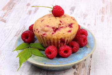 Fresh baked cupcake and raspberries on plate on old wooden background, delicious dessert