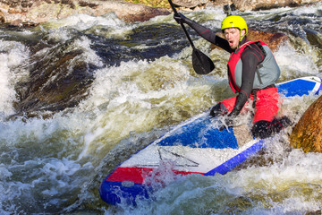 The man supsurfing on the rapids of the mountain river