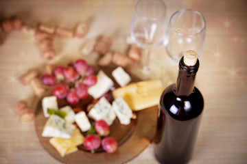 Bottle of red wine with a corkscrew on the background of different snacks of cheese and fruit