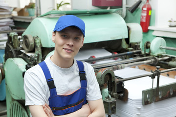 Young man in cap working on offset printing machine
