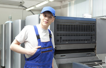 Young man in cap working on offset printing machine