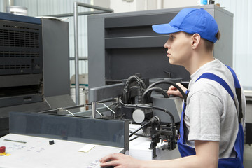 Young man in cap working on offset printing machine