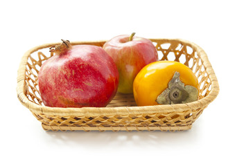Pomegranate, apple and persimmon in a wicker basket on a white background