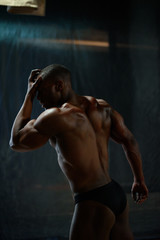 Obraz premium Portrait of handsome african american male body builder with naked torso posing on a black studio background.