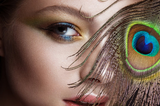 Beautiful girl with bright colored makeup and peacock feather on her face. Beauty. Close-up