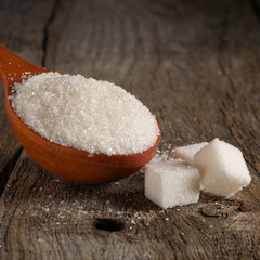 white sugar in wood spoon with sugar cubes closeup