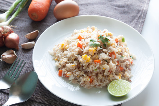 A dish of fried rice, carrot and egg on brown fabric, spoon, fol