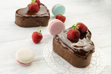 Heart cake and french macarons. Pieces of chocolate cake with fresh strawberry on wooden background.
