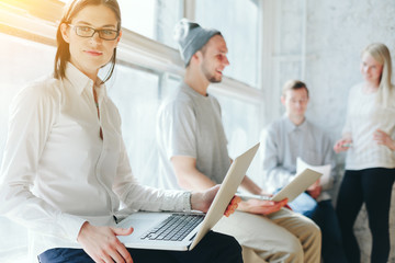 Obraz premium Coworking process. People working in big loft office. Laptop and paperwork. Intentional sun glare