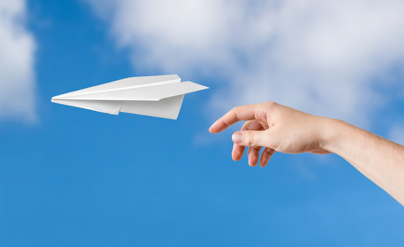Hand is throwing origami paper airplane. Blue sky on background.