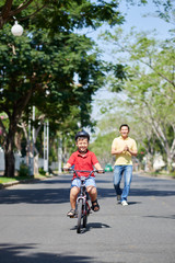 Asian man supporting his kid riding a bike for the first time