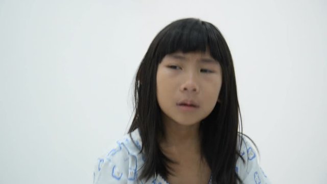 Crying Asian girl in pajamas with gray wall 