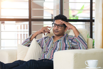 casual indian male with phone on sofa looking angry