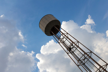 An old rusty water tower over a cloudy blue sky.