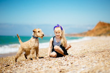 Little girl with blond hair walking on the beach with a puppy terrier 