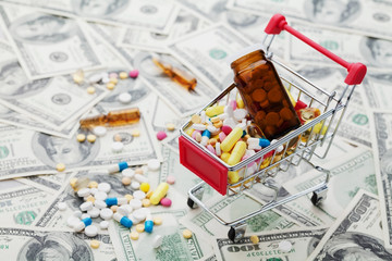 Shopping cart full of drug and medicine pills on dollar money background, pharmaceutical cost concept