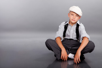 Old fashioned boy sitting on gray background