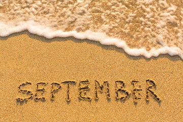 September -  written on sandy beach with the soft wave.