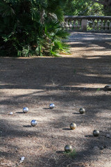 Steel balls for a game of boules on the ground among light and shadow in a subtropical park.