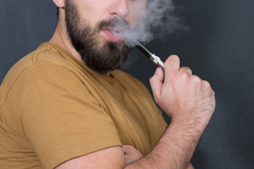 Fototapeta premium Black haired handsome man vaping e-cirarette mod - blowing cloud
