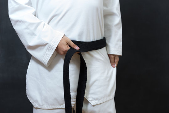 karate man tying the knot to his black belt on black background