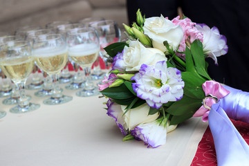 Rows of champagne glasses on table with beautiful bouquet on colorful tablecloth and rustic wooden wall at background. Wedding ceremony