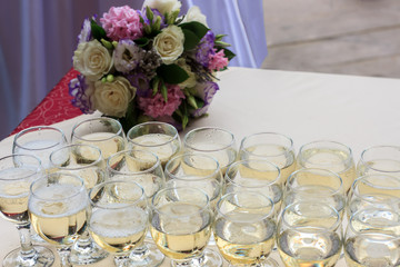 Rows of champagne glasses on table with beautiful bouquet on colorful tablecloth and rustic wooden wall at background. Wedding ceremony