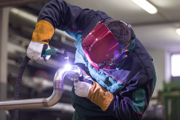 Industrial worker with protective mask welding inox elements in steel structures manufacture...