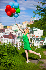 Happy young woman in green dress holding colorful balloons and flying over a panorama of old Kiev, Ukraine