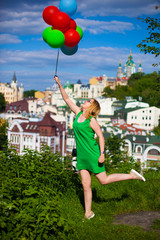 Happy young woman in green dress holding colorful balloons and flying over a panorama of old Kiev, Ukraine