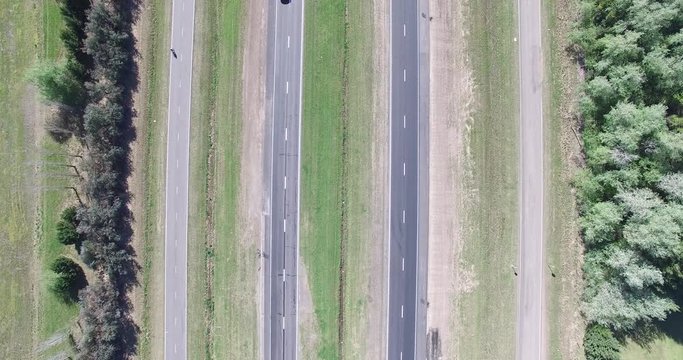 Top aerial scene of highway on the field. Trucks, motorcycle and cars movement is registered on the road. Comera stays still.