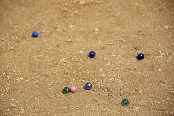 Marble balls on sand background. Croquet mallet on sand background. Playing equipment for children. Sport for children. Leisure time equipment. Coloured glass marbles. Sunny leisure time situation.