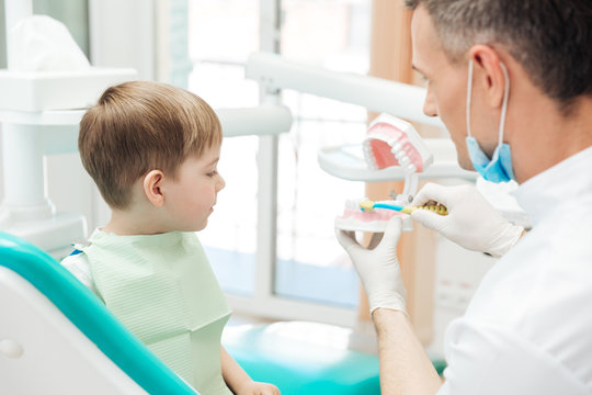 Dentist Educating Little Boy About Brushing Teeth In Clinic