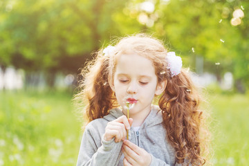 Curly girl blowing white dandelion